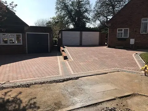Block paved driveway with a short brick dividing wall leading to garages