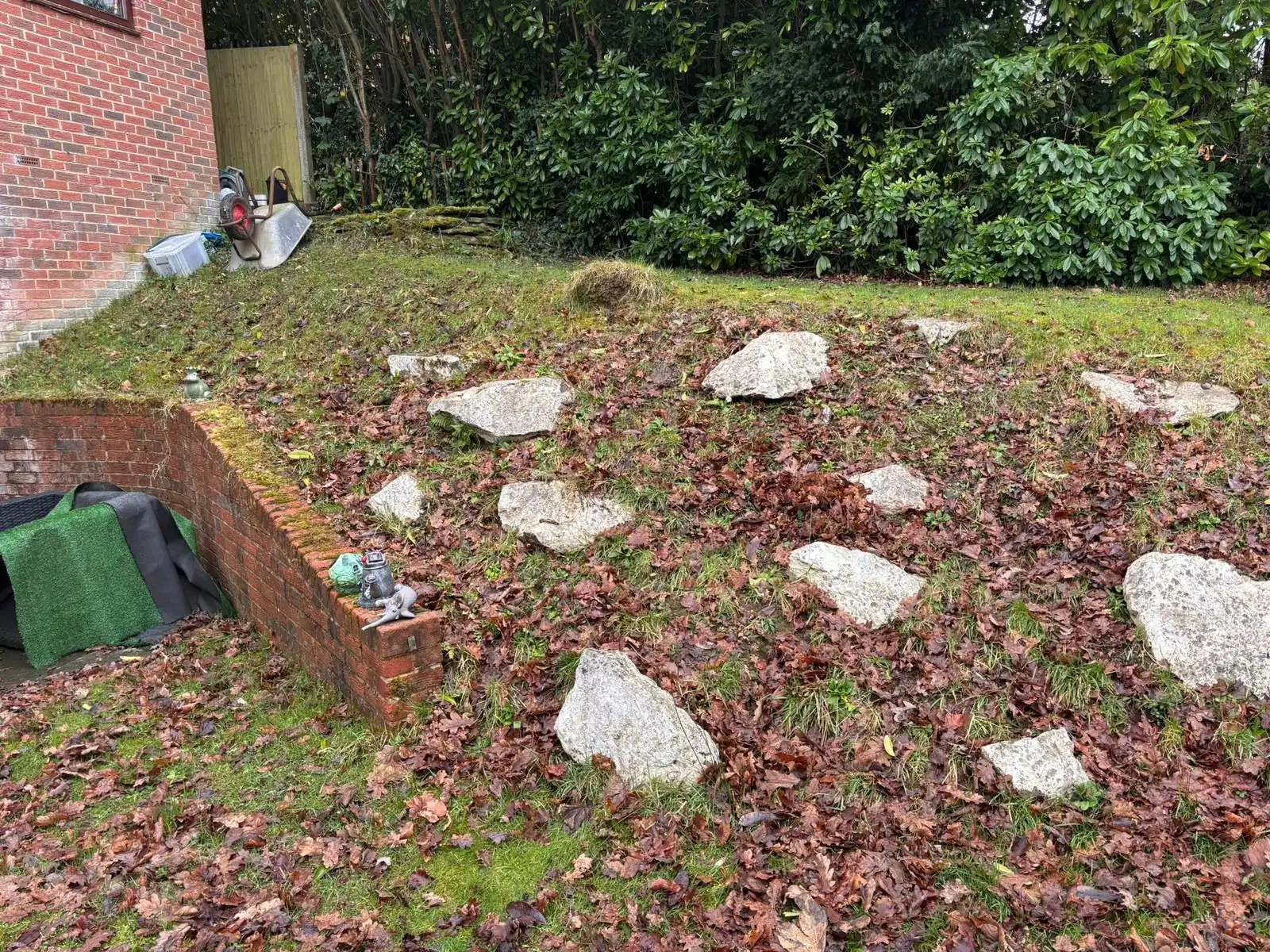 Sloping garden bed with boulders and fallen autumn leaves beside a low brick wall