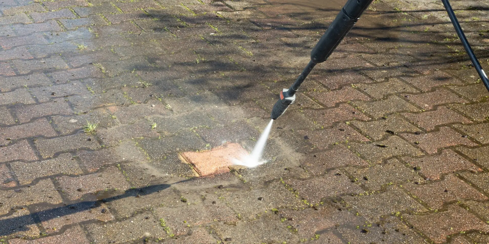 Pressure washer cleaning a strip of dirty block paving