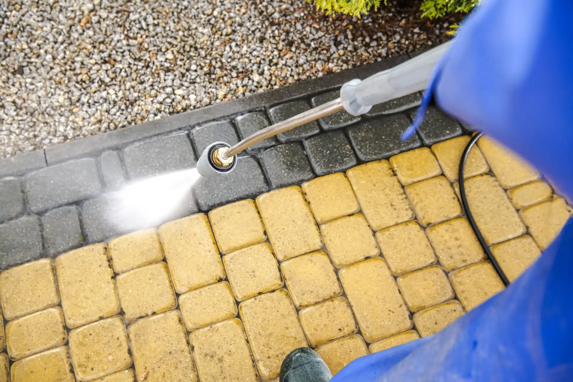 Gloved hand using a pressure washer on yellow block paving