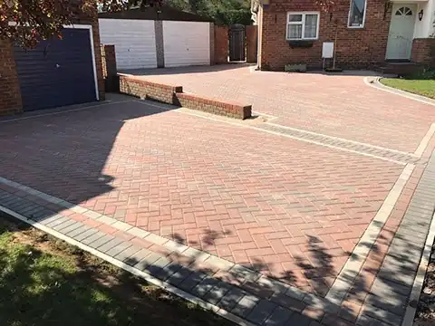 Red herringbone driveway with a low brick dividing wall in front of garages