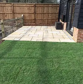 Sandstone patio beside freshly laid turf and a timber fence