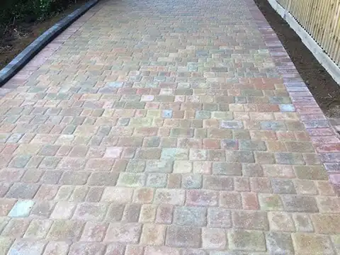 New closeboard fence running beside a tumbled block driveway